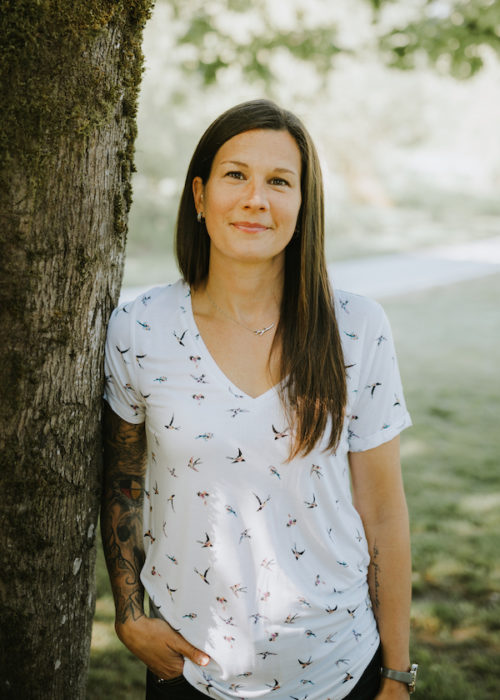 Photo of Amy Bobb standing next to a tree. Play therapist with Little Village Play Therapy.