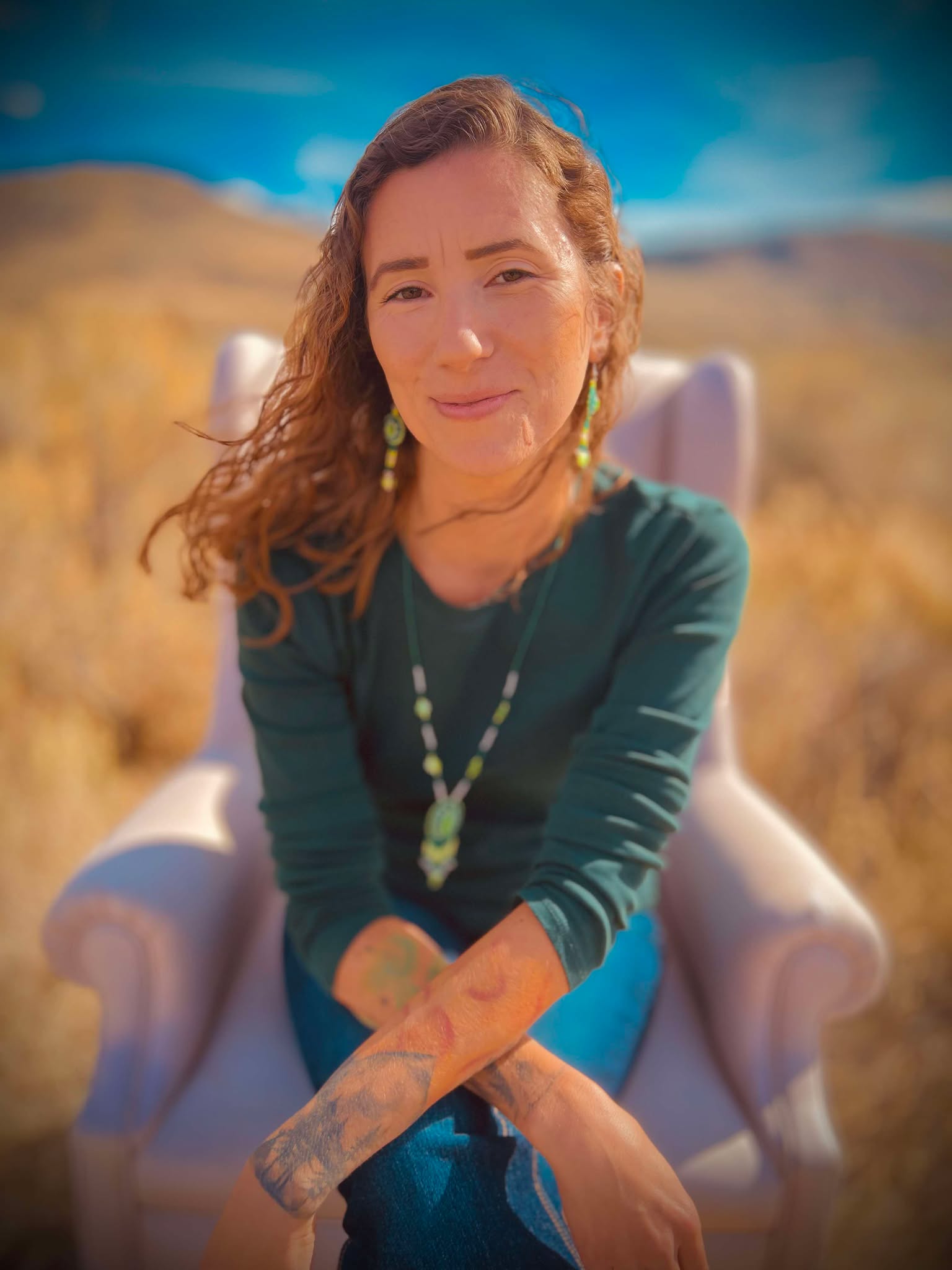 Roberta Frantzis sitting in a chair in a sage field. Wearing beadwork by Anishnaabe elder Kukom Rose
